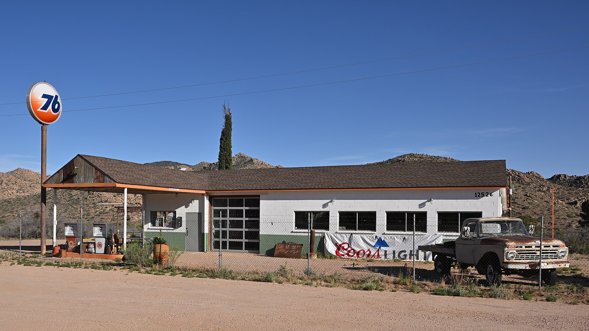 An old Union 76 gas station with the original sign, in a somewhat faded condition in front of it. On the building a sign advertises Coors Light. 12526 East Route 66, Valentine, Arizona 86437.