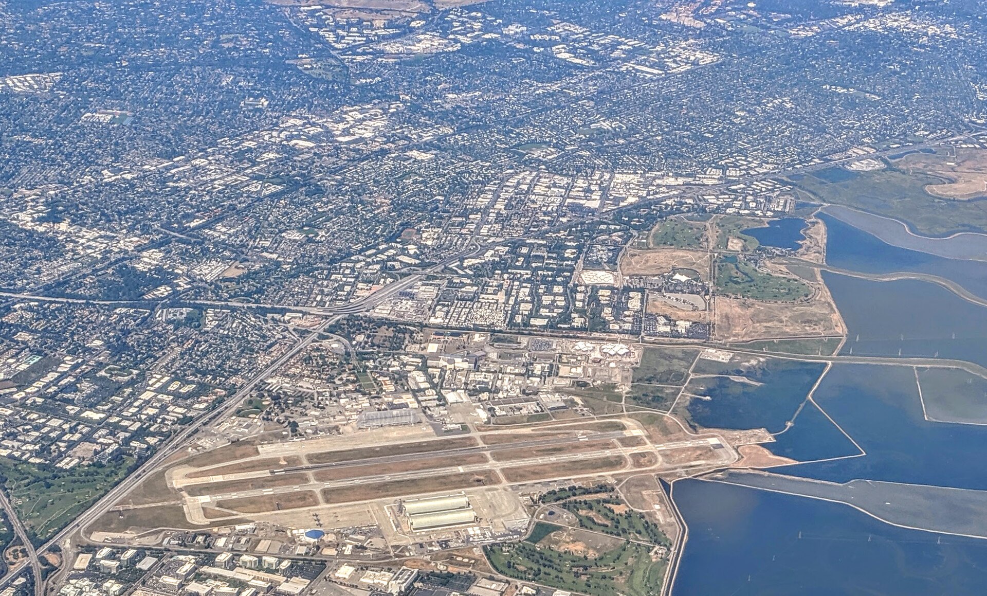 Aerial view of Moffett Field from the east, on takeoff from SJC, with new Google buildings on both sides of Stevens Creek visible beyond the field — Mountain View, California
