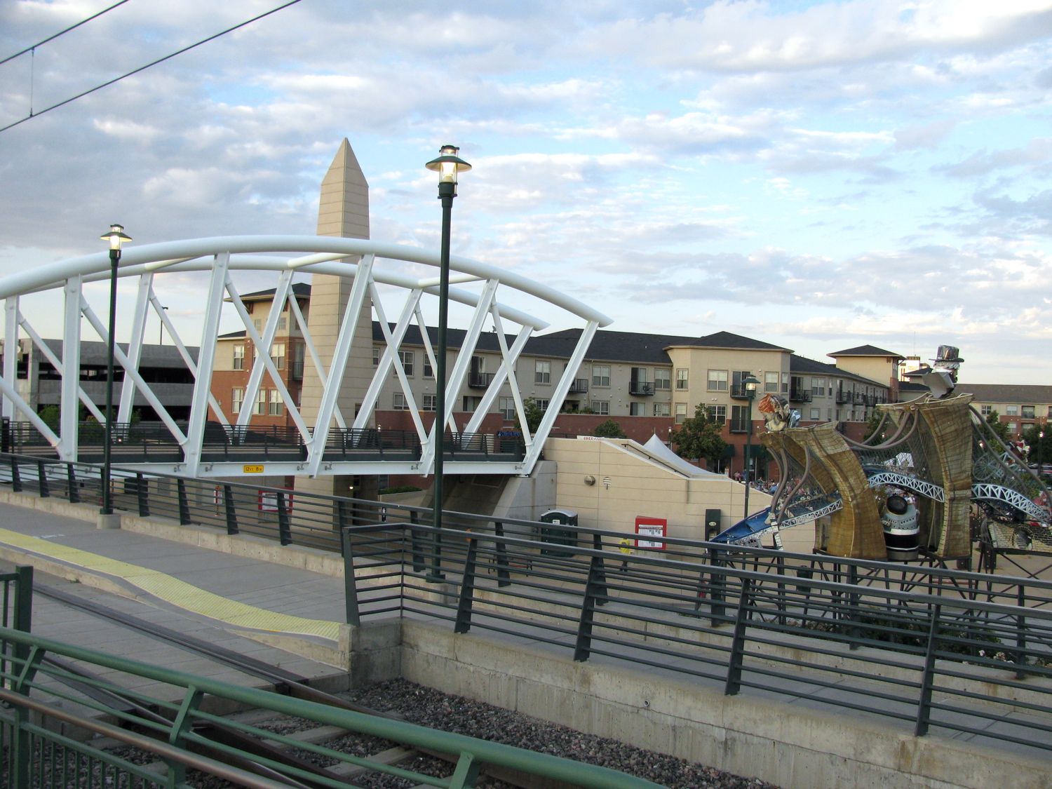 The Alexan apartments, outdoor artwork, and the RTD light rail pedestrian bridge can be seen in this picture. — Englewood, Colorado