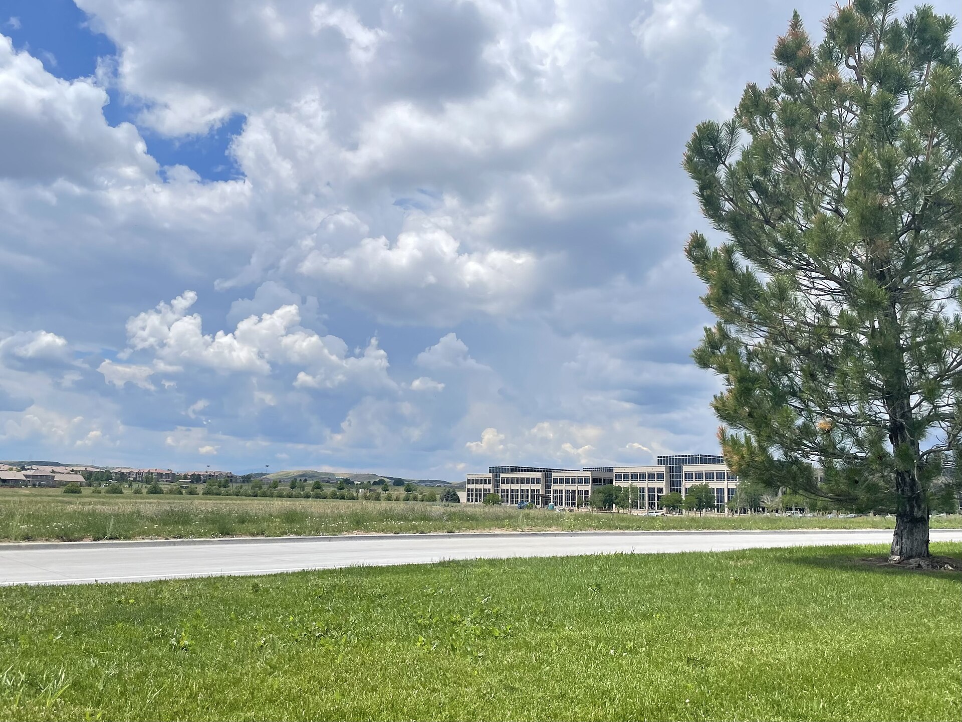 A photograph of Meridian, Colorado, on 28 June 2021. Photograph taken facing south over Belford Avenue towards the SNC building. The bluff overlooking Lone Tree can be seen in the distance.