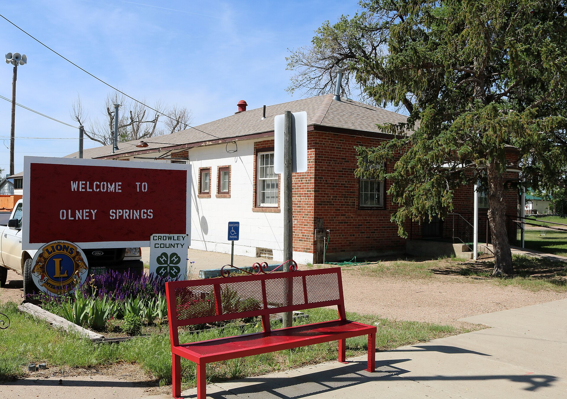 The town of Olney Springs, Colorado. The picture shows a welcome sign and the town Hall on Warner Avenue.