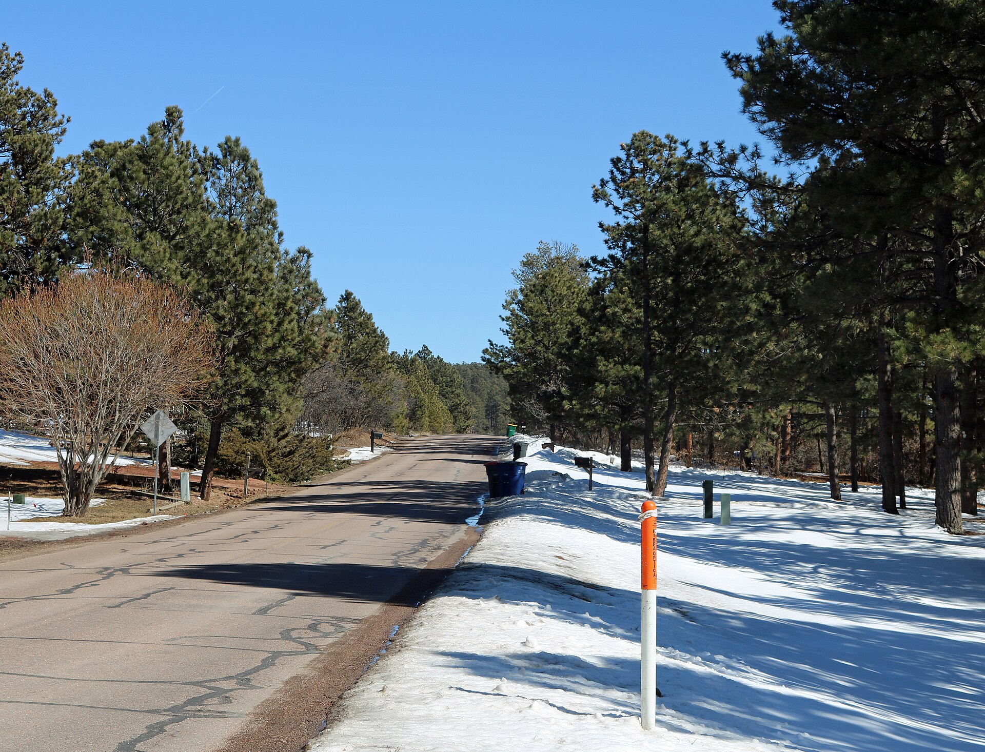 A view of Woodmoor, Colorado. The view is looking east along Woodmoor Drive from its intersection with Doewood Drive. This is a residential area of the community, which is heavily forested.