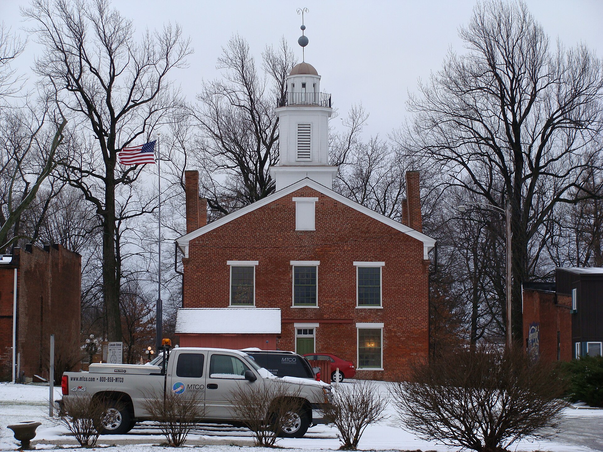 Rear of Metamora Courthouse State Historic Site seen from East Chatham Street in Metamora, Illinois, USA. In the foreground, the parking lot and utility trucks for Metamora Telephone Company (MTCO). — Woodford County, Illinois