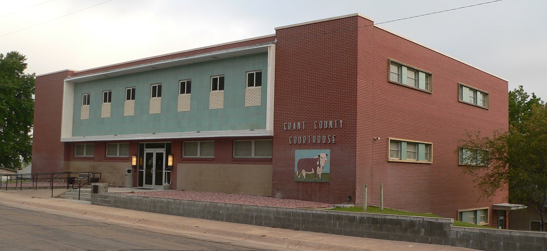 Grant County courthouse in Hyannis, Nebraska; seen from the northeast. The date 1957 appears beside the Hereford depicted on the courthouse's north wall.