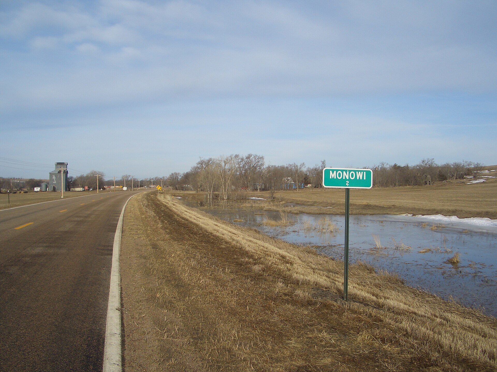 Sign announcing the population (2) of Monowi, Nebraska, USA, seen as one enters the town from the east. Some of the buildings of Monowi are visible in the background.