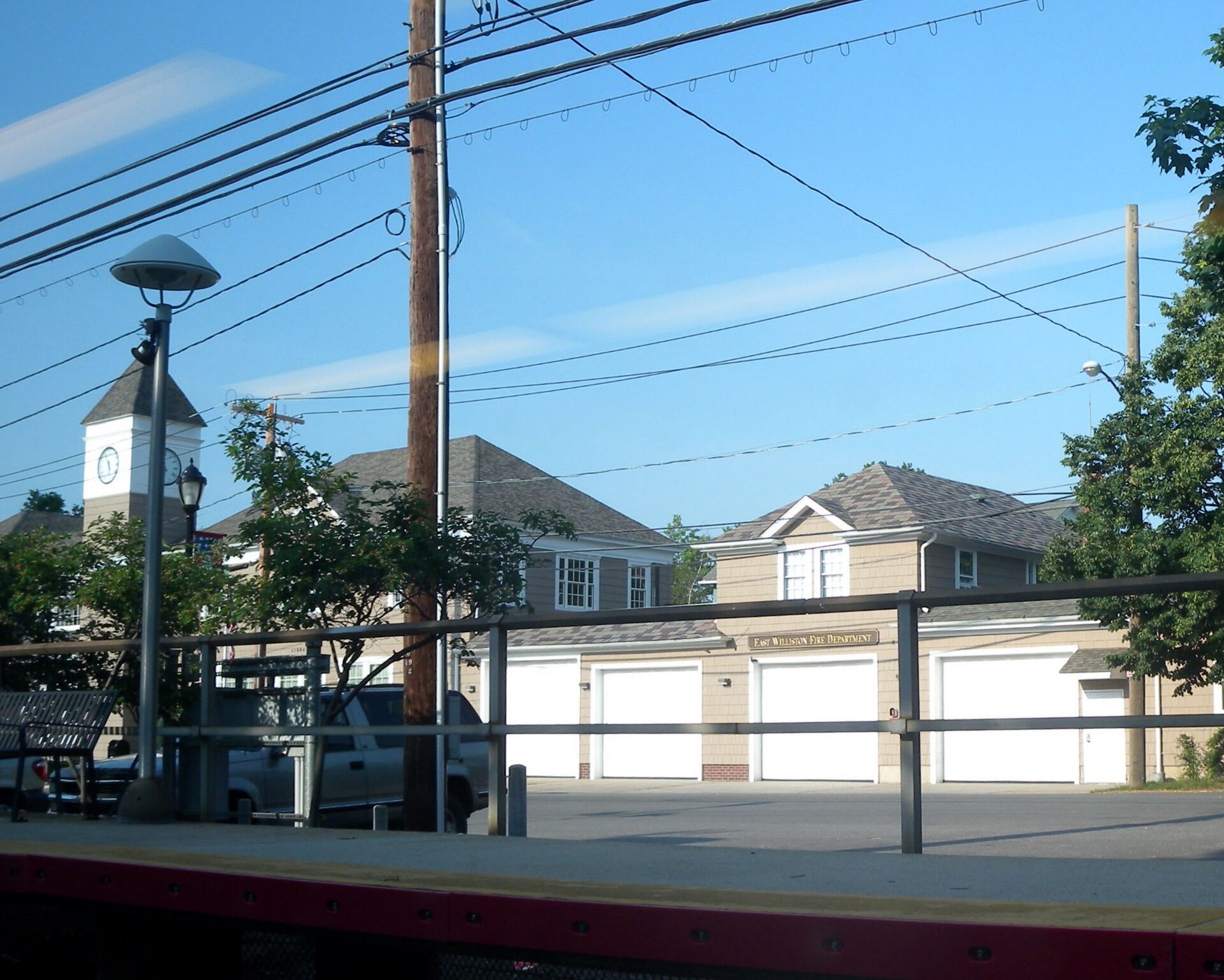 Looking northeast from a southbound train at northbound platform and East Williston Village Hall on a sunny late afternoon. — New York