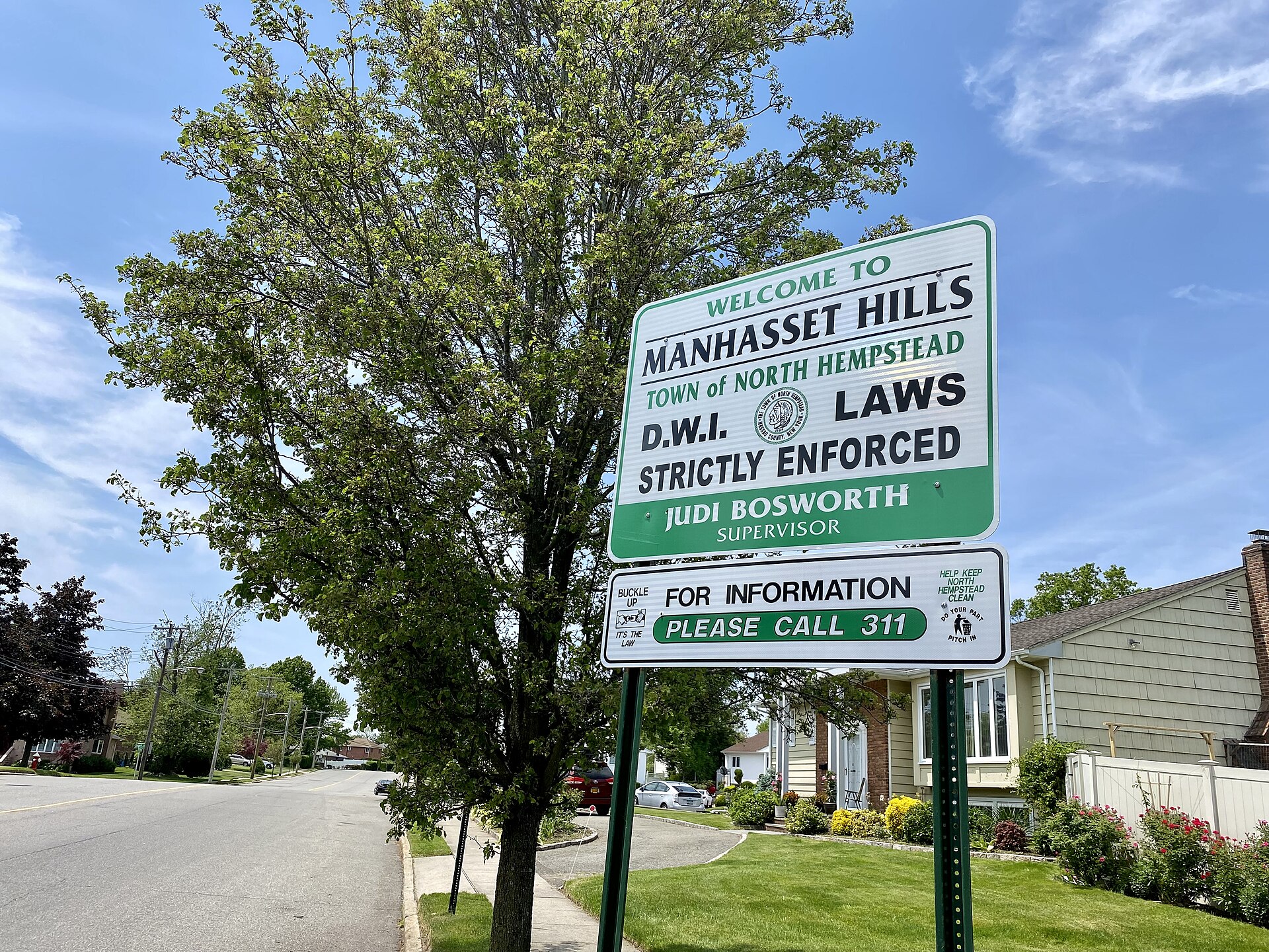A welcome sign to Manhasset Hills, Long Island, New York at the eastern end of Old Courthouse Road, at its intersection with Shelter Rock Road. This photo was taken on May 20, 2021.