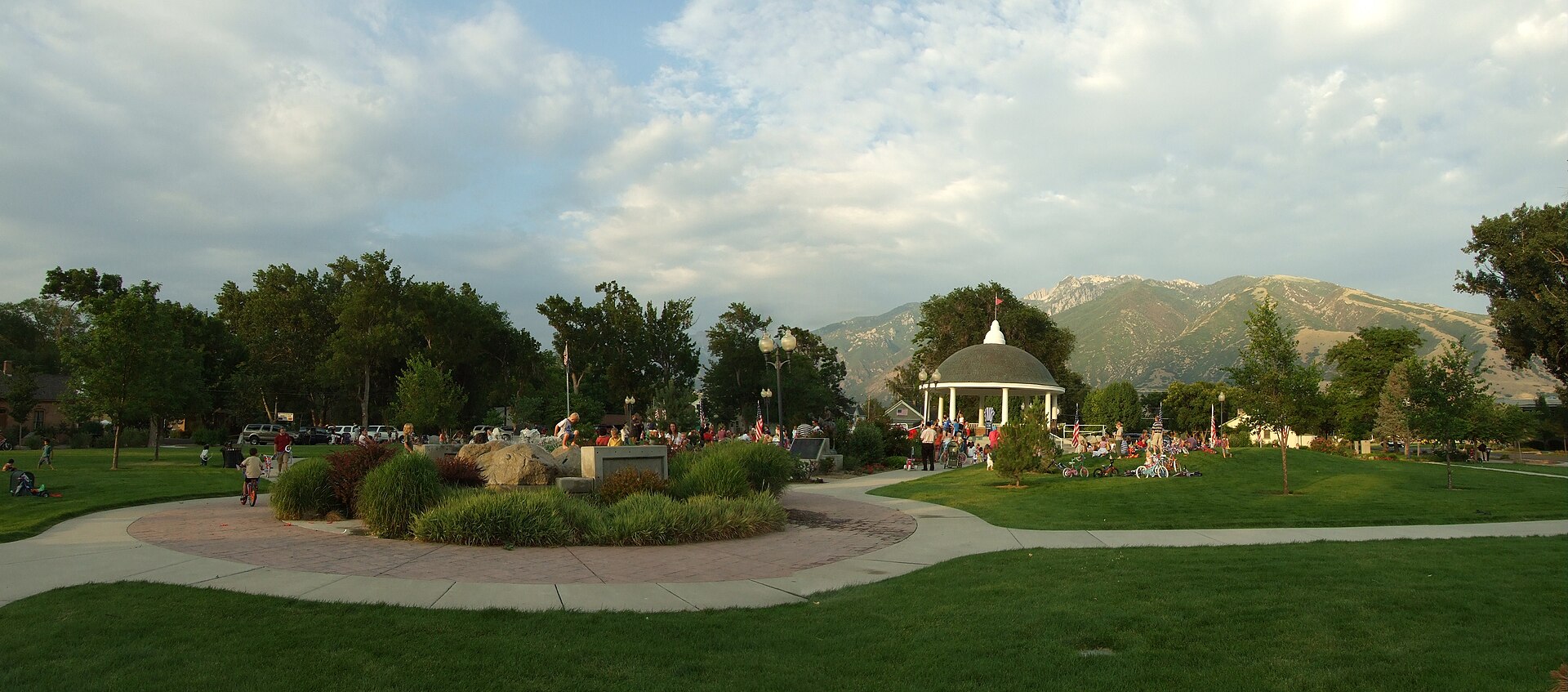 Draper Historic Park after the Draper Days Children's Parade. A magician is performing from the Gazebo. The Wasatch mountains are in the background. Stitch of two photos. July 15, 2008 — Utah