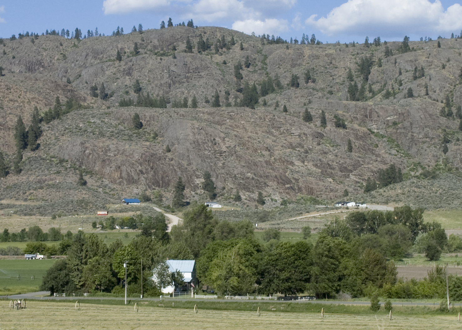 A photograph of a farmhouse outside Riverside, WA. This is along the Okanogan River and was taken from US 97. The Okanogan River, out of sight, lies between the farmhouse and the hills. — Washington